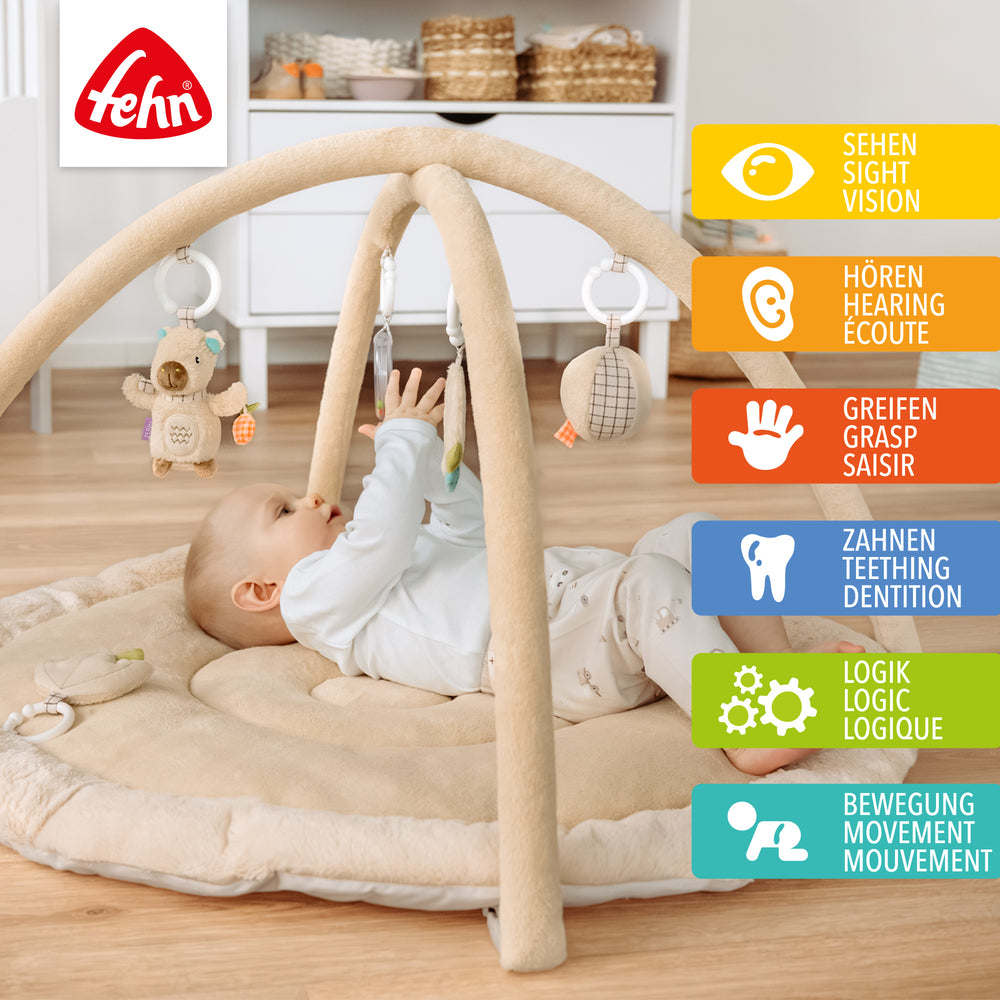 Baby liegt in Baby 3-D-Activity-Decke Capybara und greift nach Spielelement