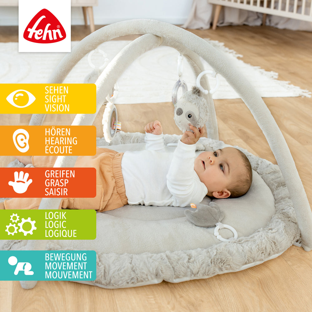 Baby liegt in Baby 3-D-Activity-Decke Faultier und greift nach Spielelement