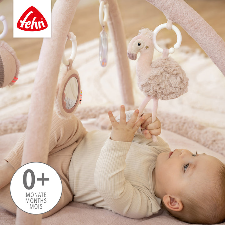 Baby liegt in Baby 3-D-Activity-Decke Flamingo und greift nach Spielelement