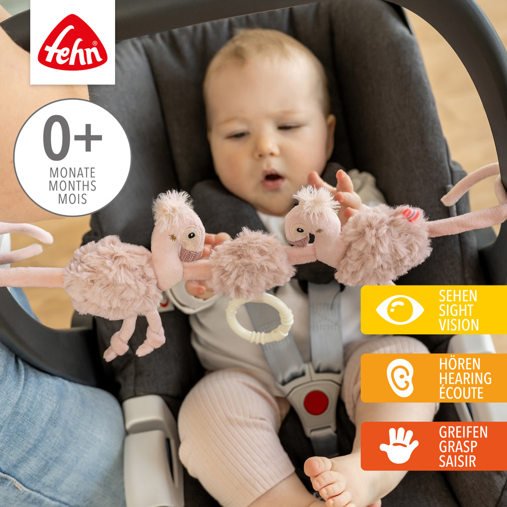Baby greift nach Baby Kinderwagenkette Flamingo aus weichem Plüsch