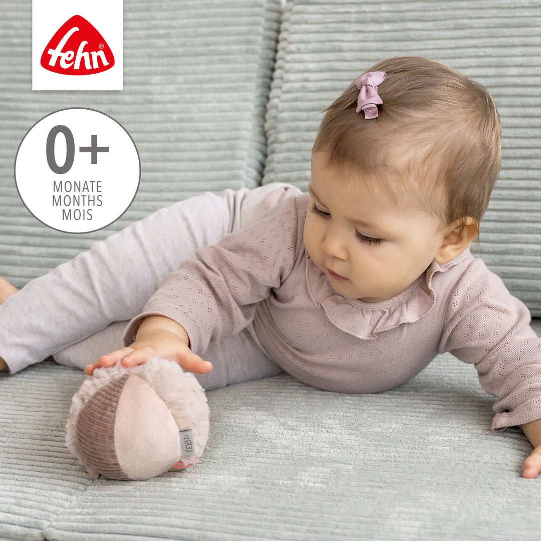 Baby greift nach Baby Stoffball Flamingo