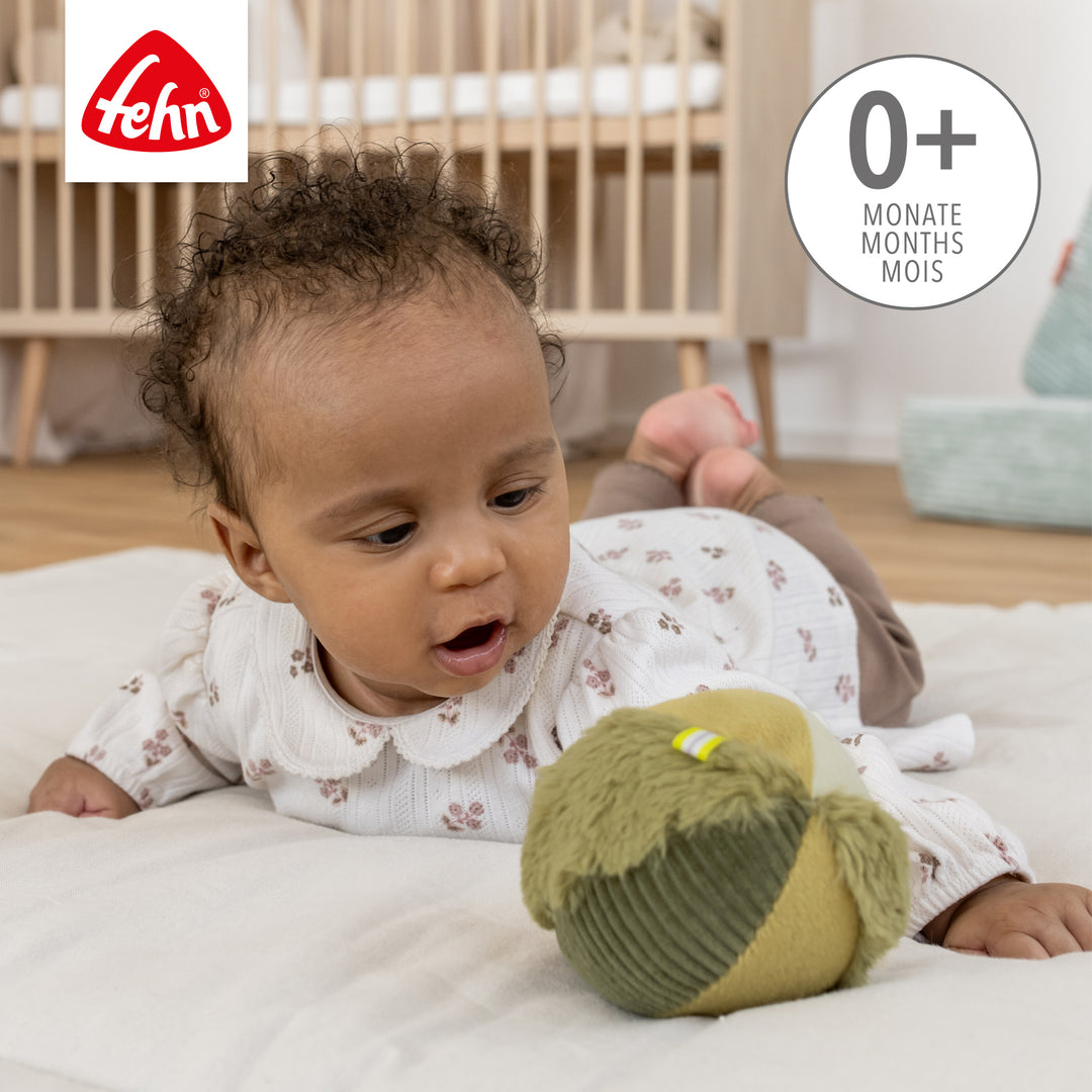 Baby greift nach Baby Stoffball Chamäleon