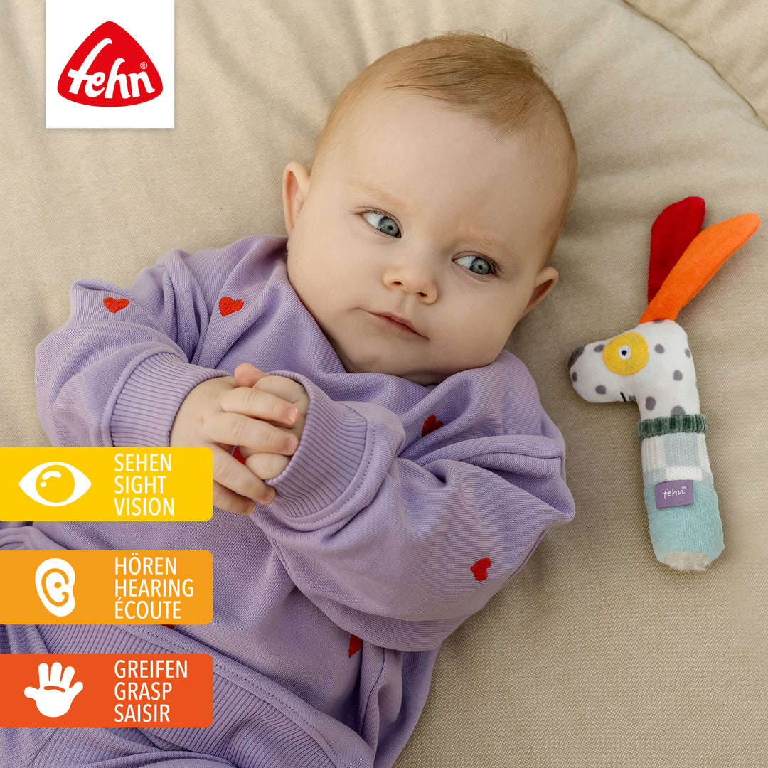 Baby spielt mit Baumwoll-Stabrassel Hund
