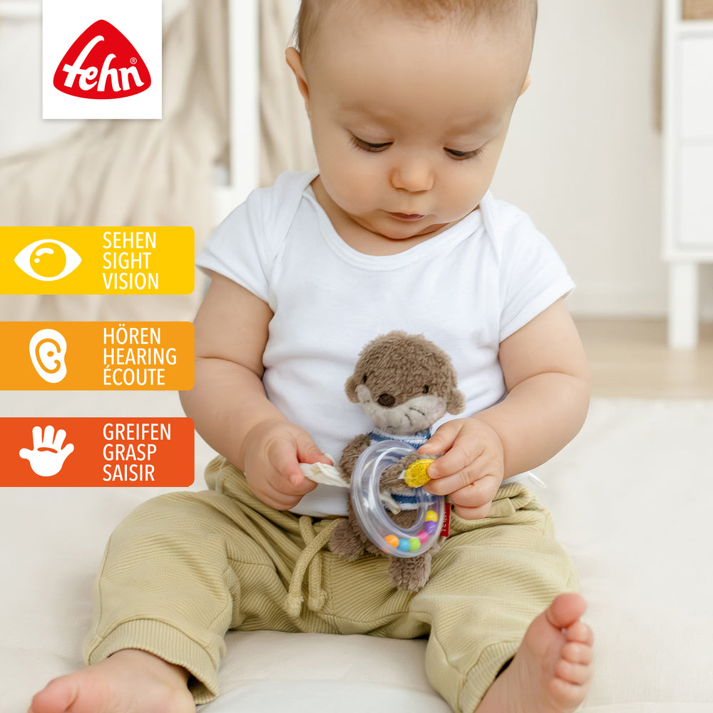 Baby hält Plüsch-Rasselring Otter